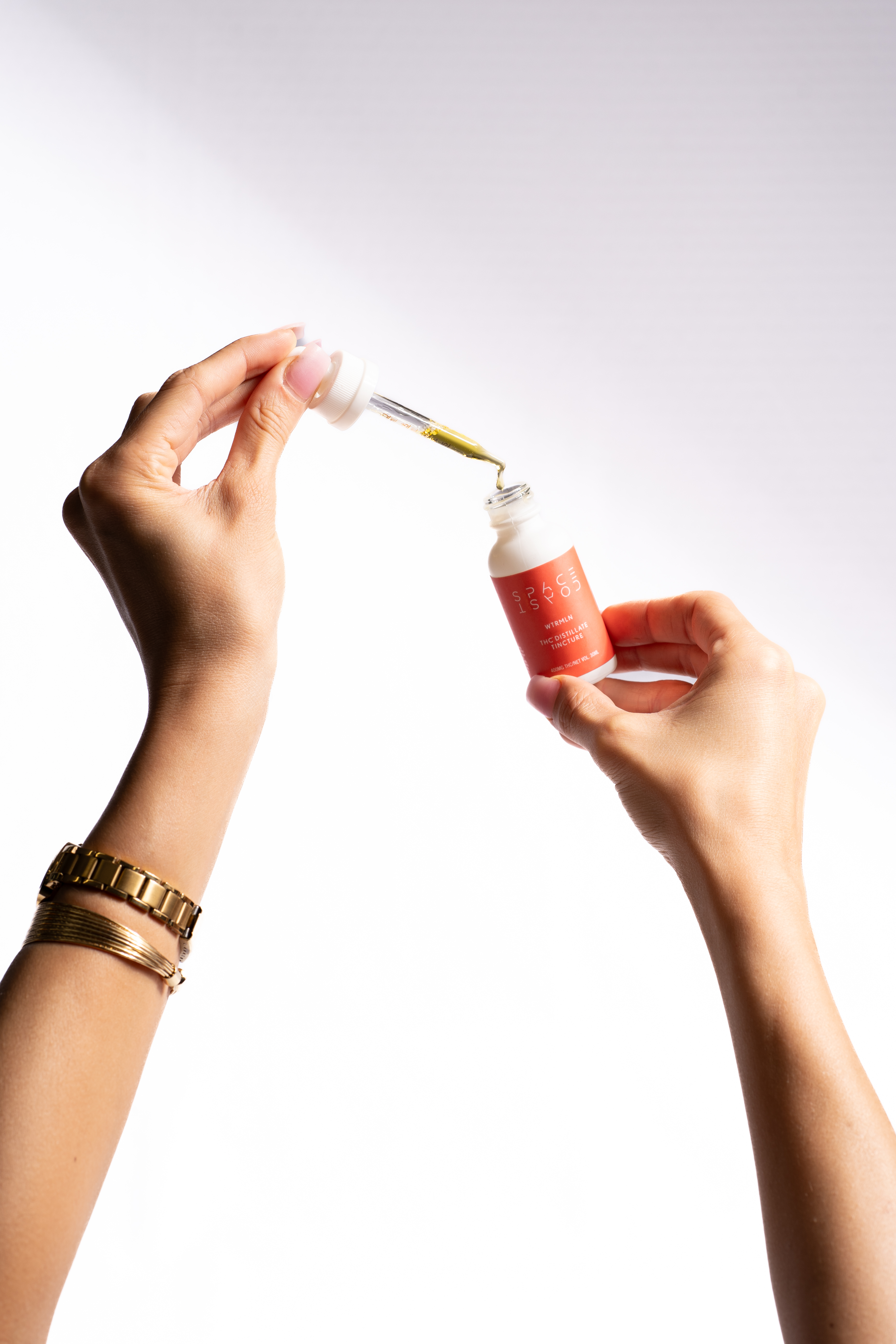 Hands holding a Space Coast THC distillate tincture bottle with the dropper above